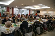 若い海兵隊員らがお年寄りの方々と一緒に感謝祭の食事。米海兵隊基地キャンプ・ハンセンに展開する第7情報大隊の隊員やその家族が11月21日（木）、七面鳥やスタッフィングなどの感謝祭を祝う典型的なアメリカの料理を持ち寄り、特別養護老人ホーム光が丘の利用者やスタッフ総勢100名余りで感謝祭の食事を分かち合いました。