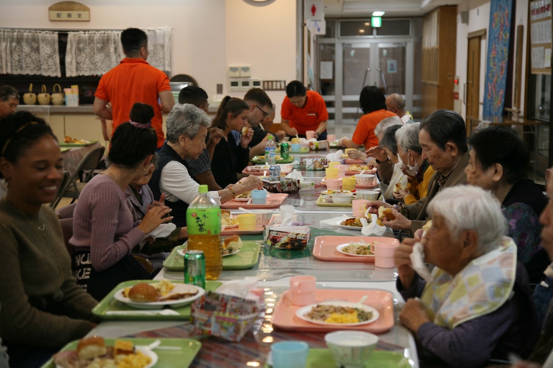 若い海兵隊員らがお年寄りの方々と一緒に感謝祭の食事。米海兵隊基地キャンプ・ハンセンに展開する第7情報大隊の隊員やその家族が11月21日（木）、七面鳥やスタッフィングなどの感謝祭を祝う典型的なアメリカの料理を持ち寄り、特別養護老人ホーム光が丘の利用者やスタッフ総勢100名余りで感謝祭の食事を分かち合いました。