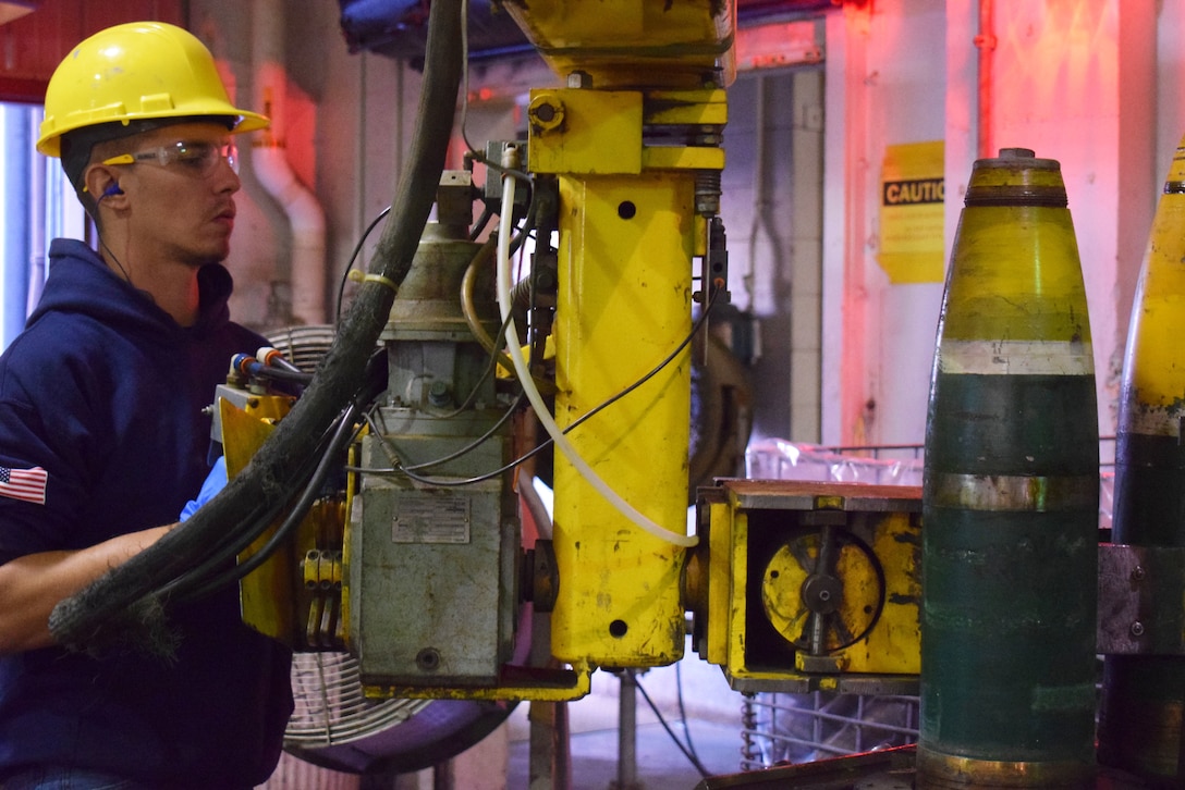 A man in a hard hat uses machinery to move munitions.