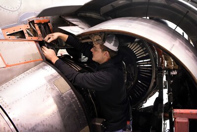 A man in a hard hat uses machinery to move munitions.