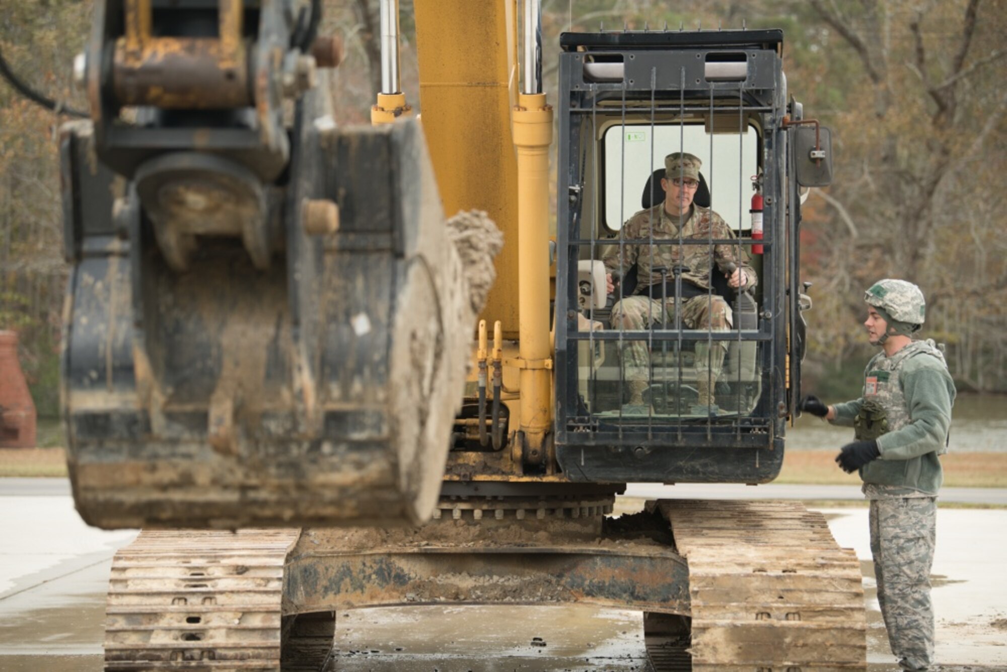 U.S. Air Force Col. Mark D. Piper, 192nd Wing commander, operates a backhoe with the help of Senior Airman Seth Price, 203rd RED HORSE Squadron heavy equipment operator, during a field training exercise on Nov. 16, 2019, at State Military Reservation, Virginia Beach, Virginia. More than 150 Airmen participated in the exercise to practice skills they would perform in a deployed environment. (U.S. Air National Guard photo by Senior Airman Bryan Myhr)