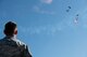 A Creech Airman watches Special Operations Command Para-Commandos parachute during the opening ceremony of Aviation Nation, at Nellis Air Force Base, Nevada, Nov. 16, 2019. The SOCOM Para-Commandos performed a parachute demonstration during the opening ceremonies of Aviation Nation. (U.S. Air Force photo by Staff Sgt. Omari Bernard)