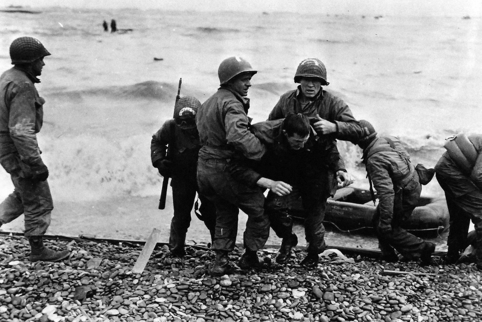 Members of American landing party carry comrades ashore from life raft somewhere in Northern France after their landing craft was sunk, June 6, 1944 (U.S. Army Signal Corps)