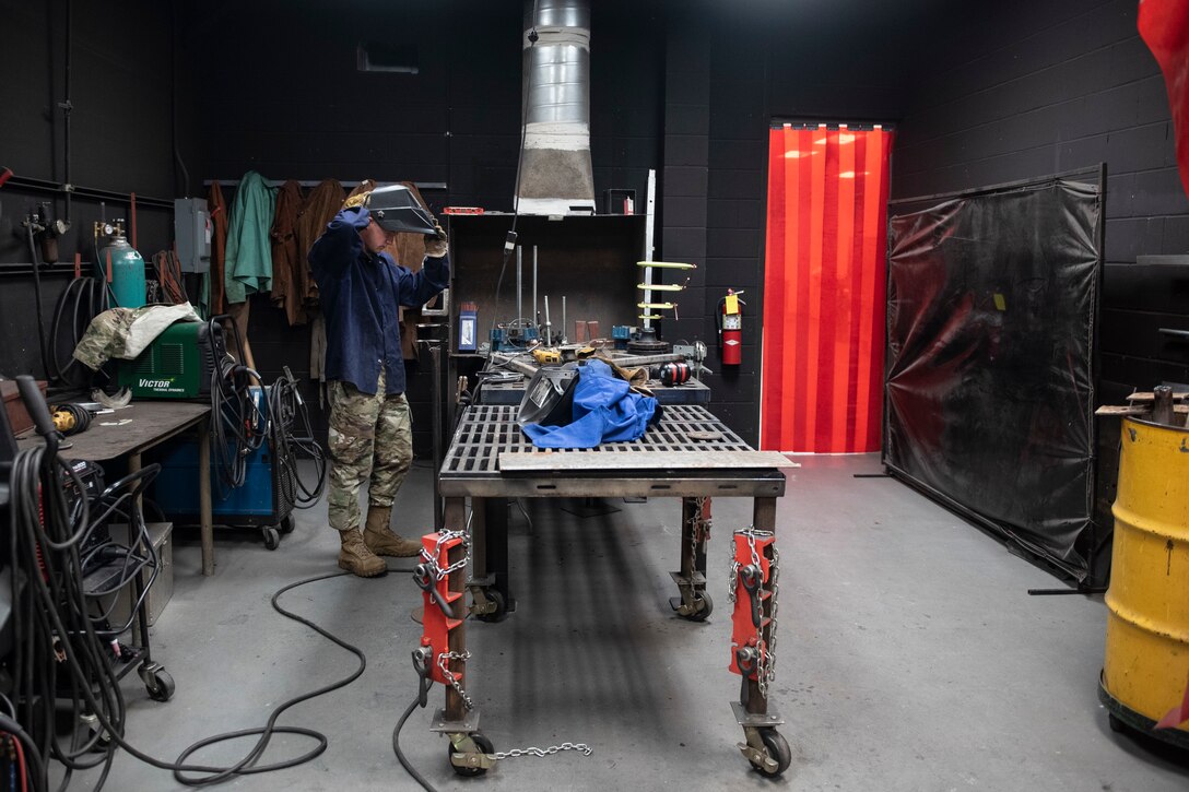A photo of an Airman donning protective gear before welding a handrail