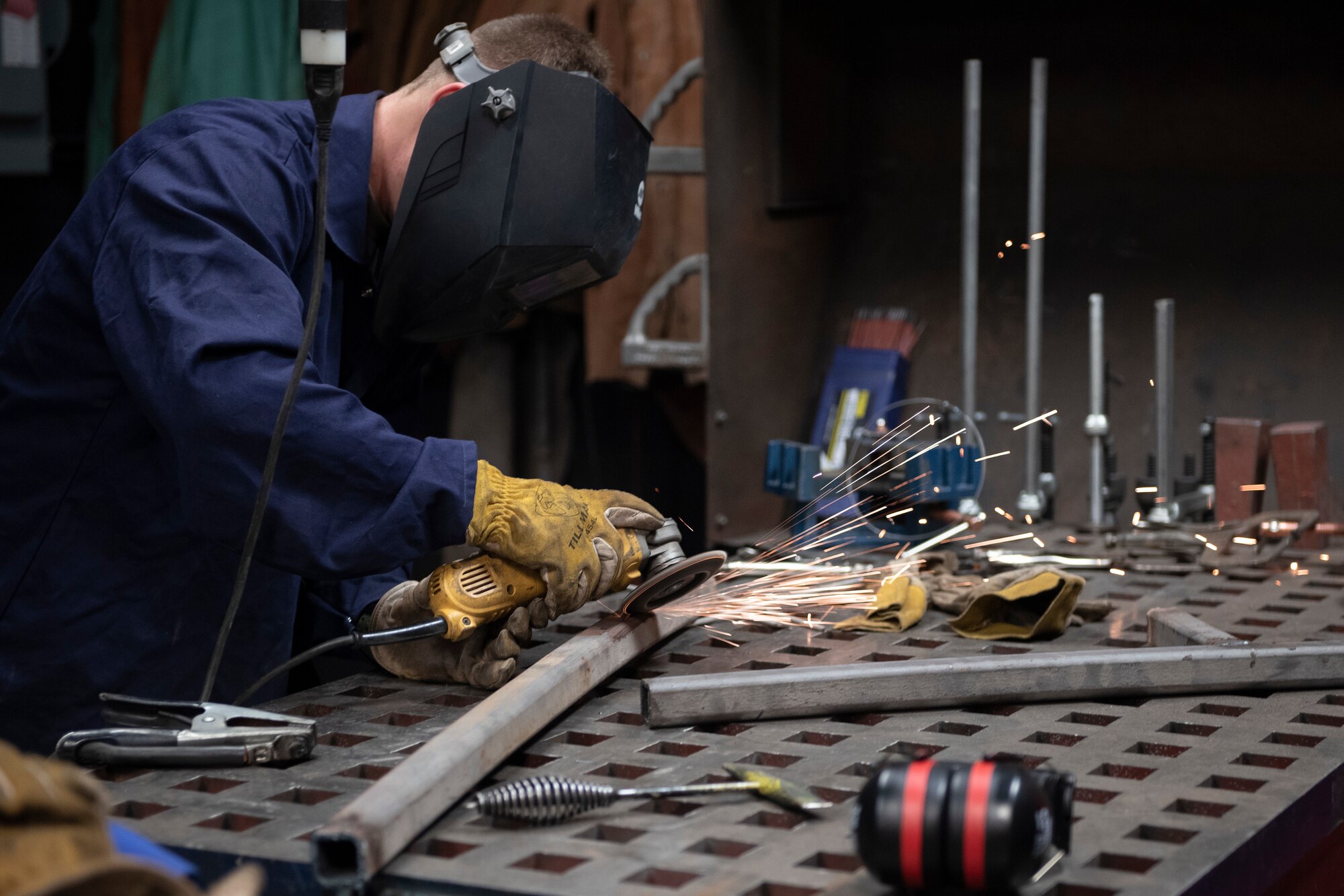 A photo of an Airman grinding metal to clear it of rust before welding