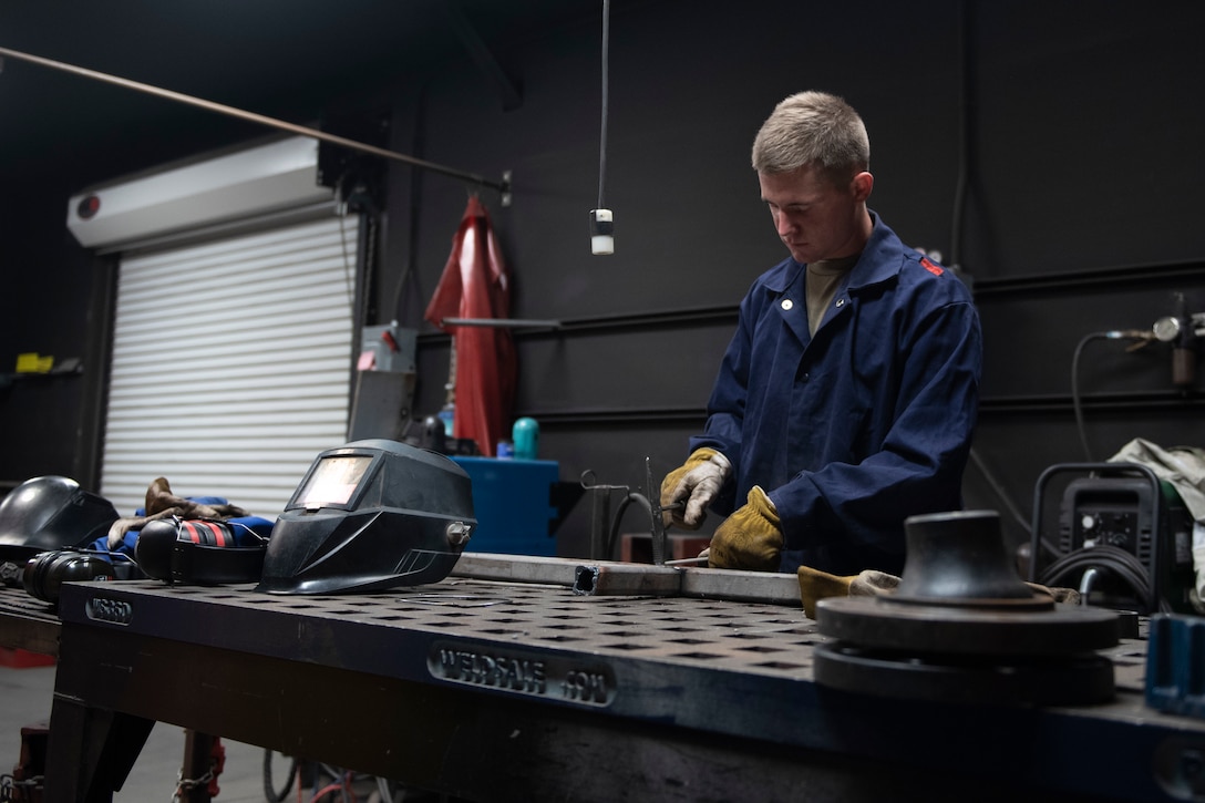 A photo of an Airman using a chipping hammer to remove slag before welding metal
