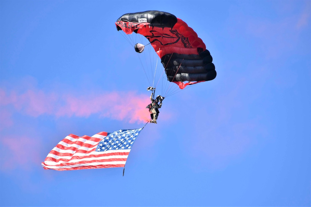A soldiers descends through the sky holding an American flag.