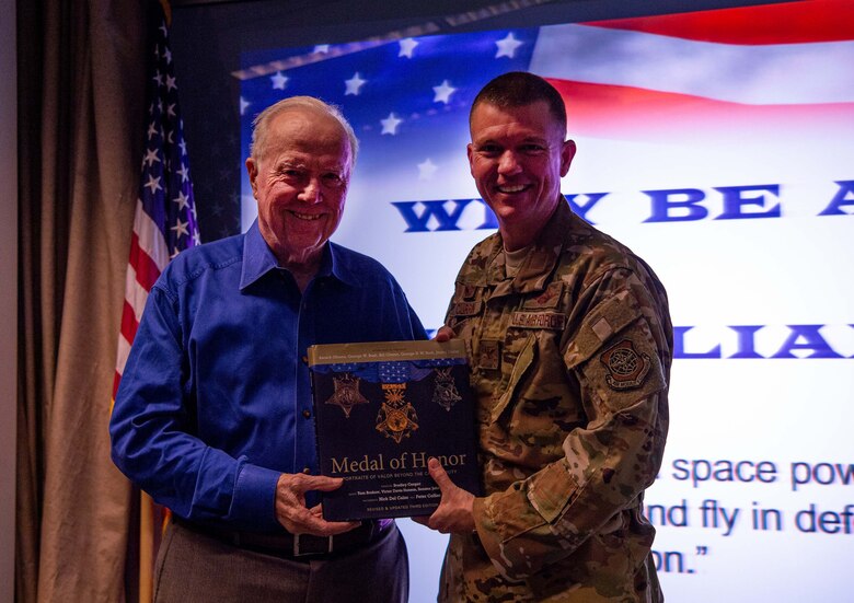 Retired U.S. Army Col. Bruce Crandall, a Medal of Honor recipient, right, presents the book Medal of Honor to U.S. Air Force Col. Scovill Currin, 62nd Airlift Wing commander, left, at Joint Base Lewis-McChord (JBLM), Wash., Nov. 21, 2019. Crandall visited JBLM to talk about his time in the Army during a professional development presentation. (U.S. Air Force photo by Senior Airman Tryphena Mayhugh)