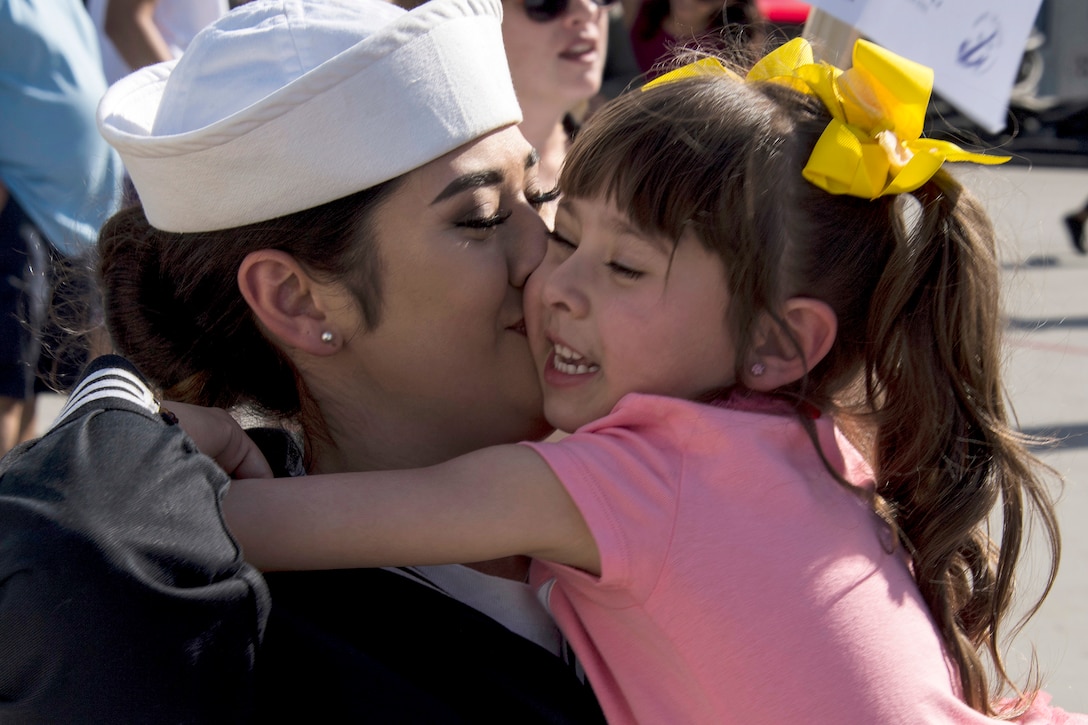A sailor kisses a smiling child she holds in her arms.