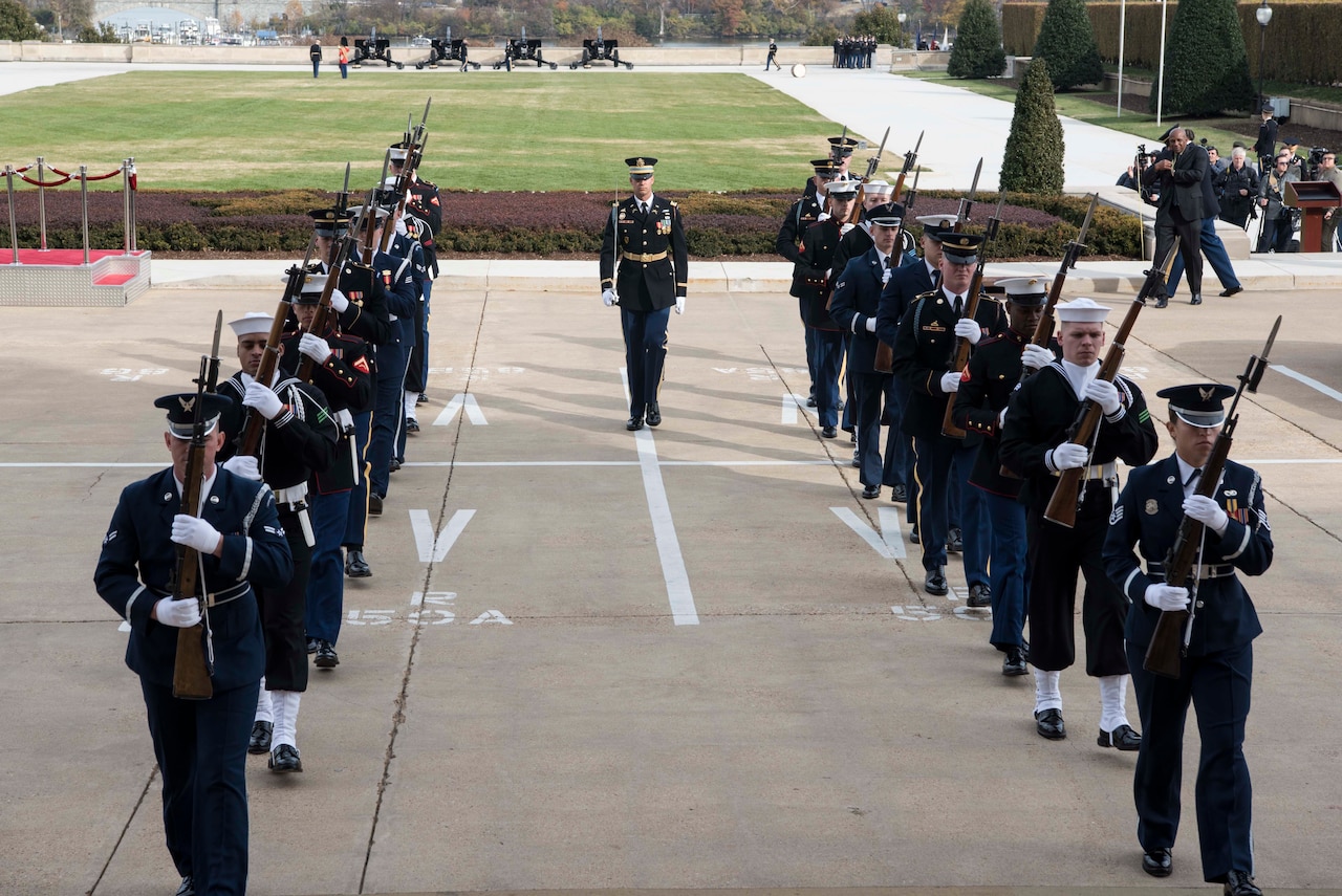 Service members carrying rifles stand in two rows.