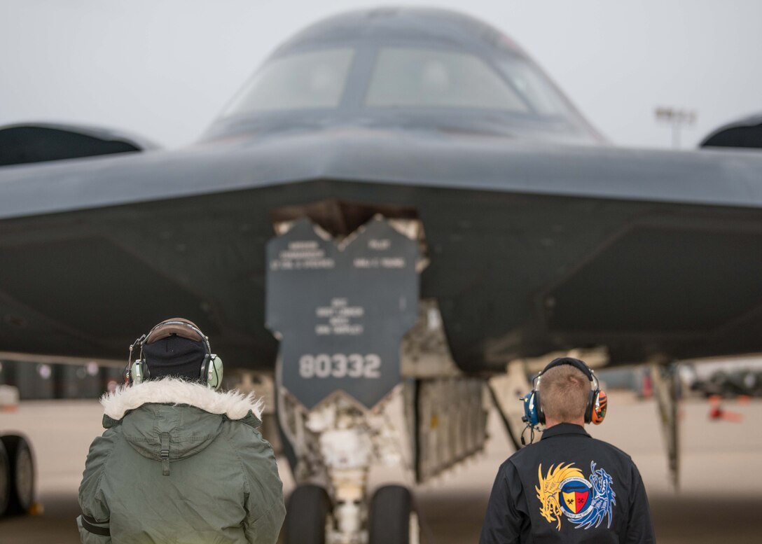 A view of the back of two crew chiefs who are looking at B-2 Spirit Stealth Bomber in front of them.