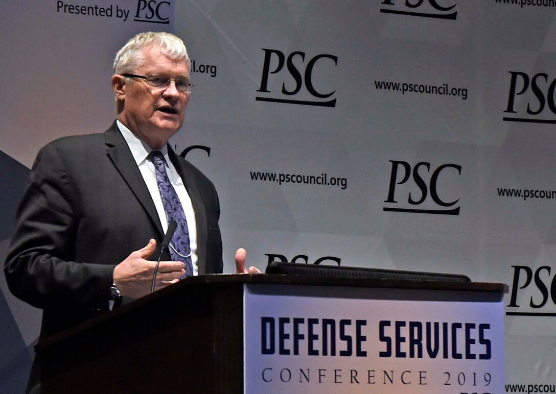 A man in a suit speaks at a podium.