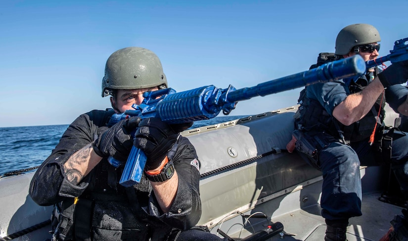 Sailors point guns from small boat.