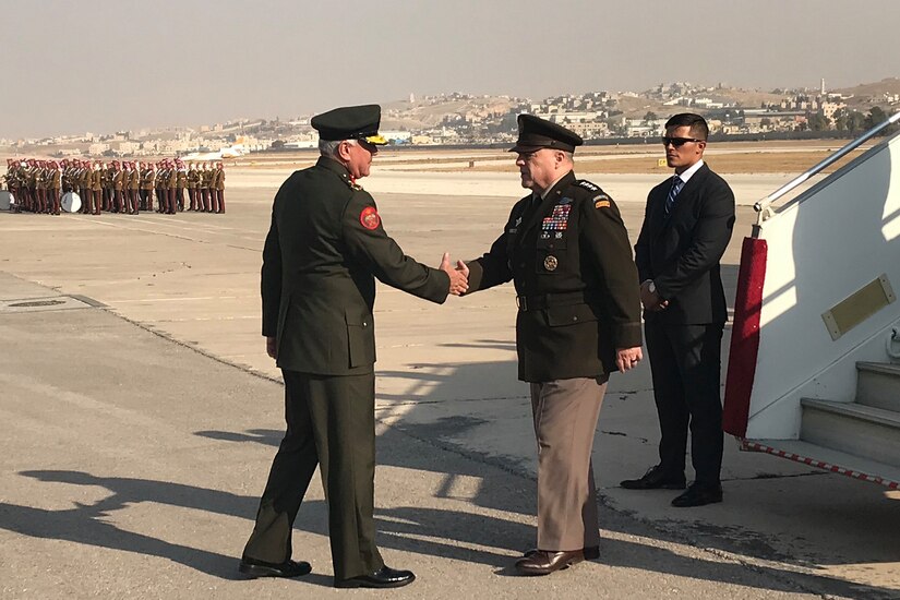 Men in service uniforms shake hands at the bottom of an airplane ramp.