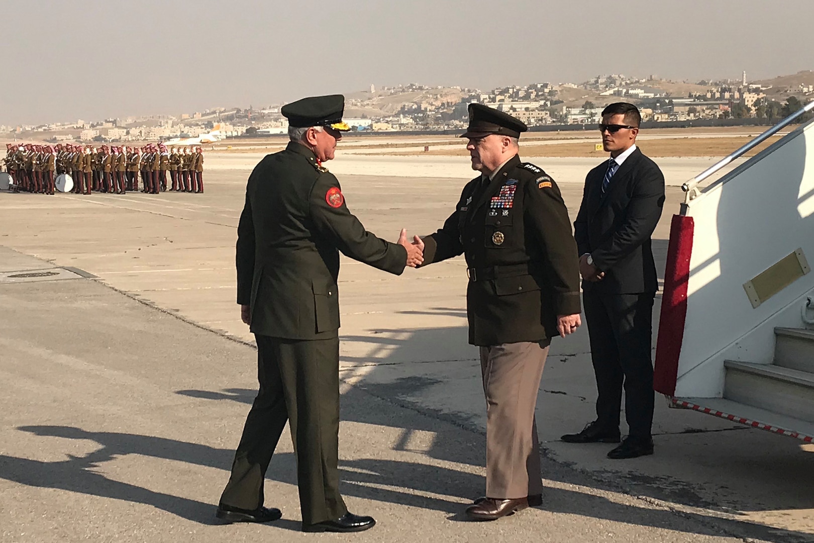 Men in service uniforms shake hands at the bottom of an airplane ramp.