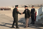 Men in service uniforms shake hands at the bottom of an airplane ramp.