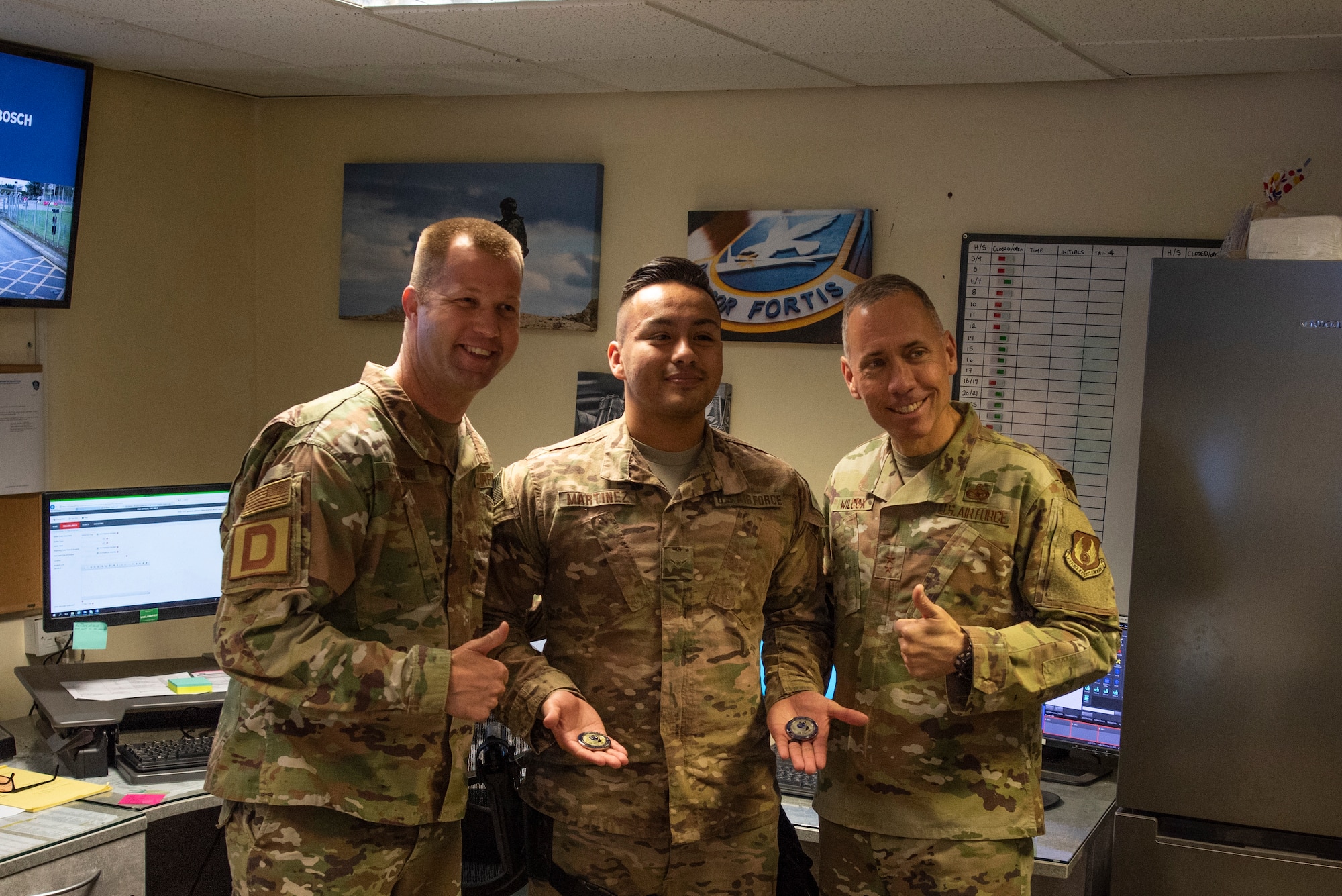 Maj. Gen. John Wilcox, Air Force Installation and Mission Support Center commander, and Chief Master Sgt. Edwin Ludwigsen, AFIMSC command chief master sergeant, pose for a photo with Airman Anthony Martinez, 100th Security Forces Squadron base defense operations center controller, after coining him Nov. 22, 2019, at RAF Mildenhall, England. The AFIMSC provides installation and mission support that enables Team Mildenhall to complete its varied mission sets.  (U.S. Air Force photo by Airman 1st Class Joseph Barron)