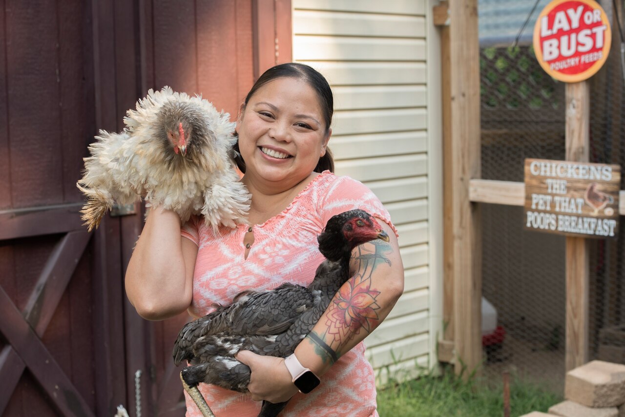 Woman poses holding two chickens.
