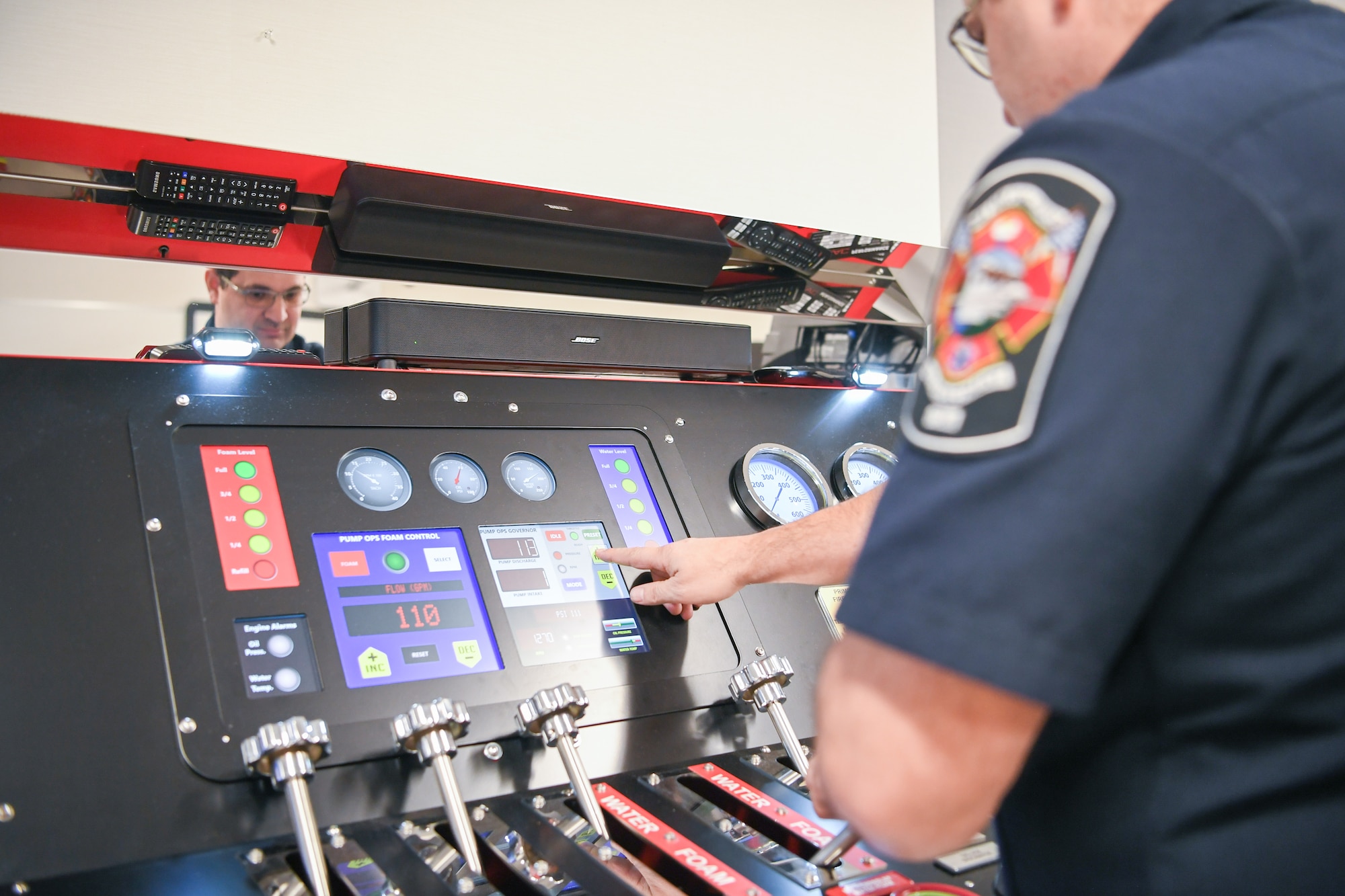 Jason Medina, Fire and Emergency Services driver operator, touches a digital screen on a pump simulator panel that is adorned with handles,dials and gauges.