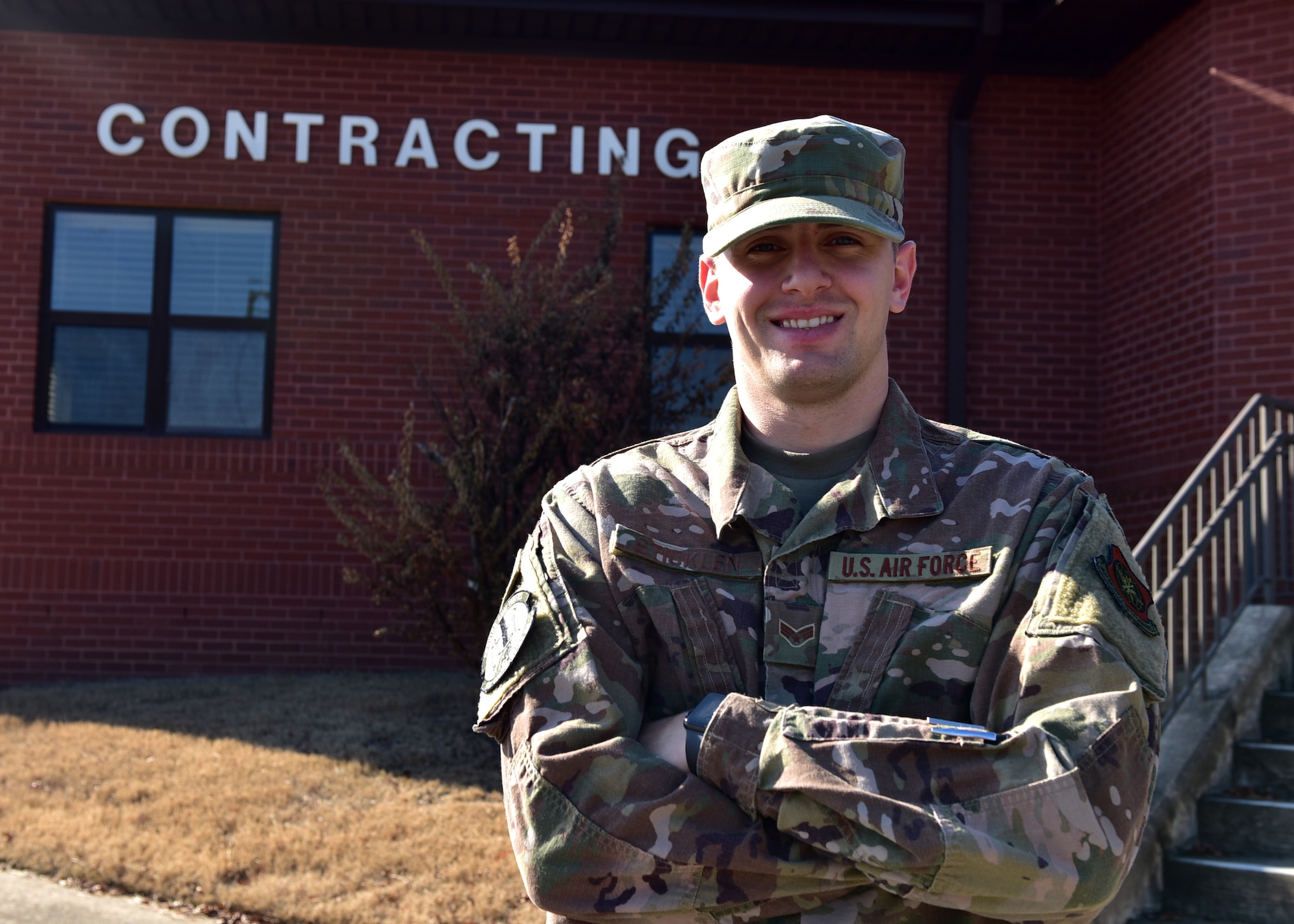 A male in uniform stands outside next to a brick building with the words "Contracting" written on the side