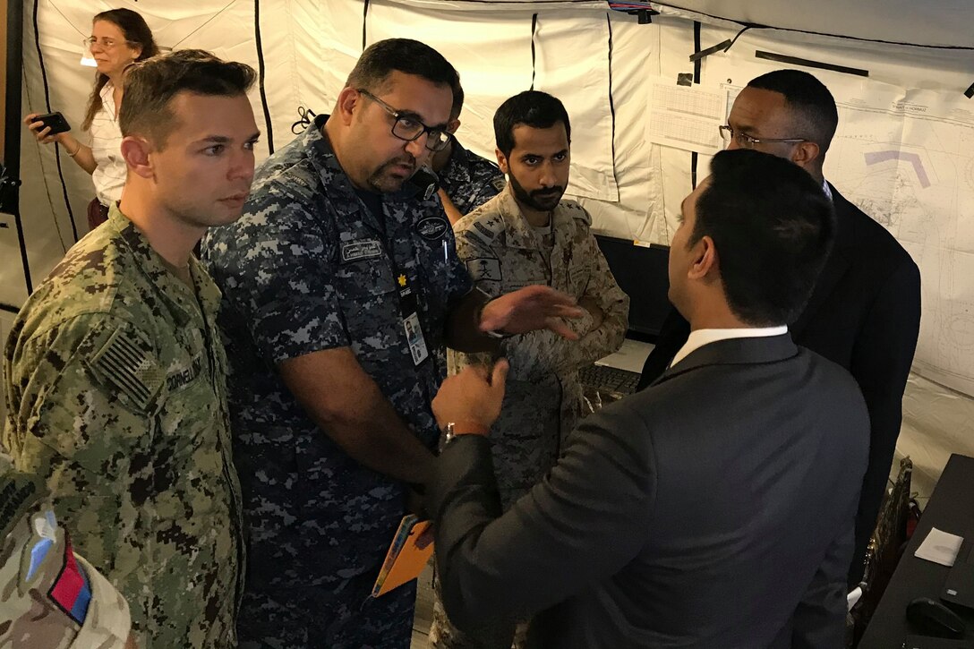 Officer in blue uniform speaks to civilians in a tent.