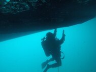 U.S. Marine Corps Lance Cpl. Patrick Roundtree, a diver with 3rd Reconnaissance Battalion, 3d Marine Division, removes hard fouling from the Keel Cooler Unit of U.S. Army Vessel Harpers Ferry at Naval Station White Beach, Okinawa, Japan, Nov. 15, 2019.