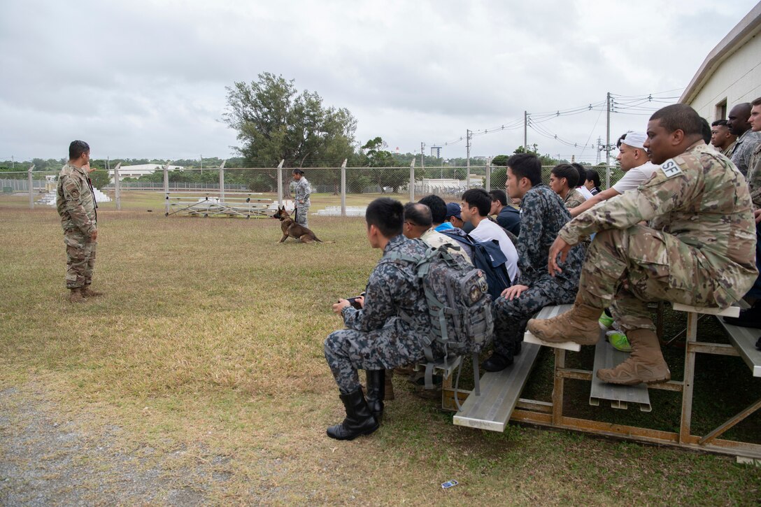 U.S. Air Force Tech. Sgt. Mario Rey, 18th Security Forces Squadron military working dog handler, left, speaks with U.S. Air Force, U.S. Army, and Japanese Self-Defense Force members participating in an NCO Bilateral Exchange program about the capabilities and training of military working dogs Nov. 18,2019, at Kadena Air Base, Japan. Bilateral exchanges allow for a better understanding of the capabilities held by each countries Armed Forces, as well as the opportunity to improve relations between the United States and Japan.(U.S. Air Force photo by Senior Airman Rhett Isbell)