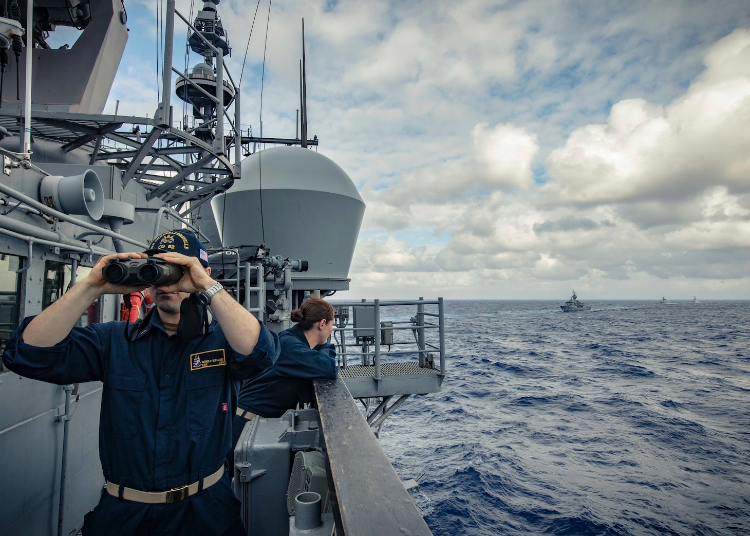 PHILIPPINE SEA (Nov. 21, 2019) Ens. Warren McWilliams looks forward as Lt. j.g. Katherine Lindman observes approaching ships on the bridge of the Ticonderoga-class guided-missile cruiser USS Chancellorsville (CG 62) during a group maneuvering exercise with ships from the Royal Australian Navy, Royal Canadian Navy, and Republic of Korea Navy as part of Pacific Vanguard 2019. Chancellorsville is forward-deployed to the U.S. 7th Fleet area of operations in support of security and stability in the Indo-Pacific region.