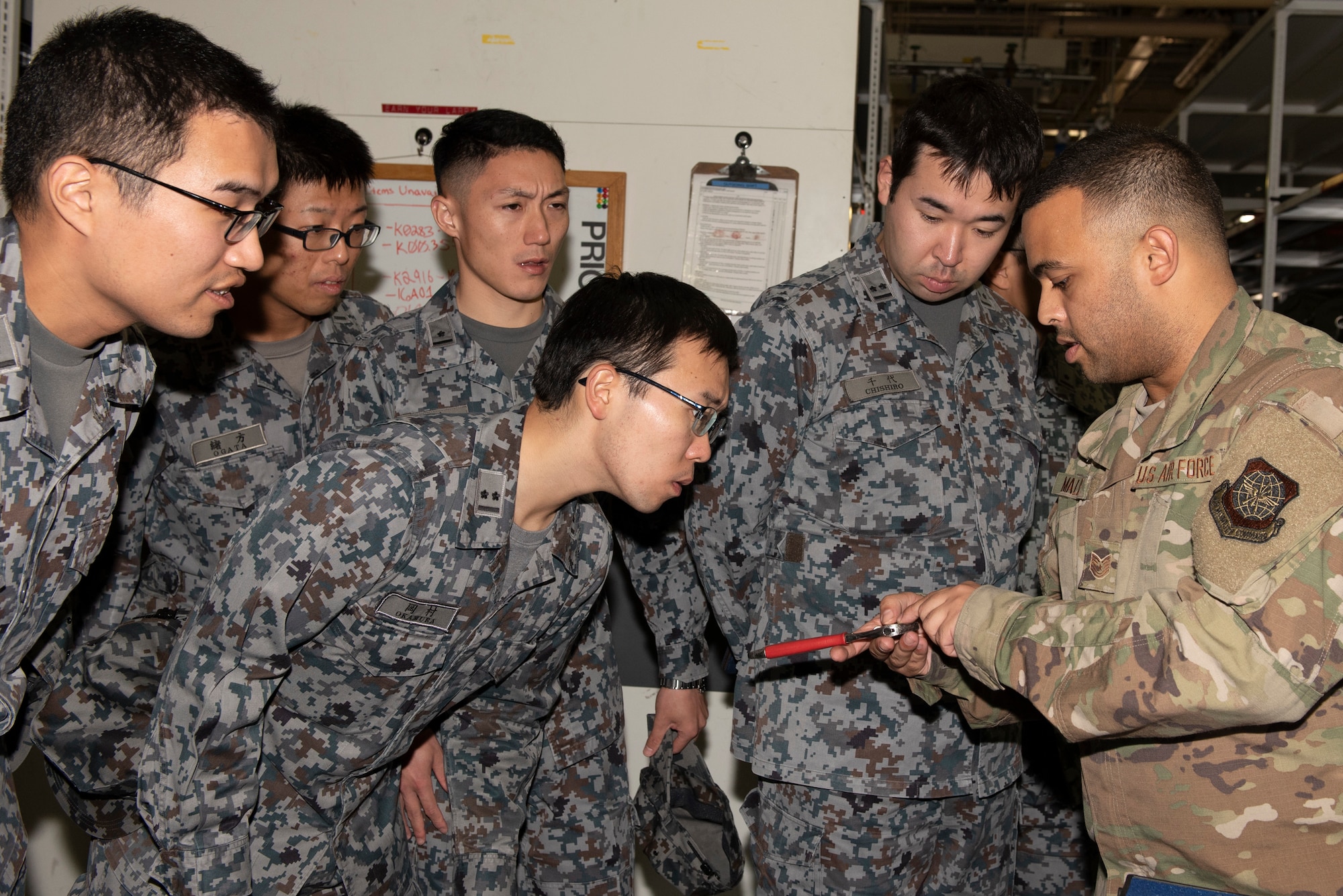 Tech.Sgt. Eliseo Malave, 730th Air Mobility Squadron NCO in charge of support, right, shows a tool engraved with an ID number to Japanese Air Self-Defense Force Lieutenants at the 730 AMS composite tool kit support section during a basic maintenance officer tour at Yokota Air Base, Japan, Nov. 21, 2019.