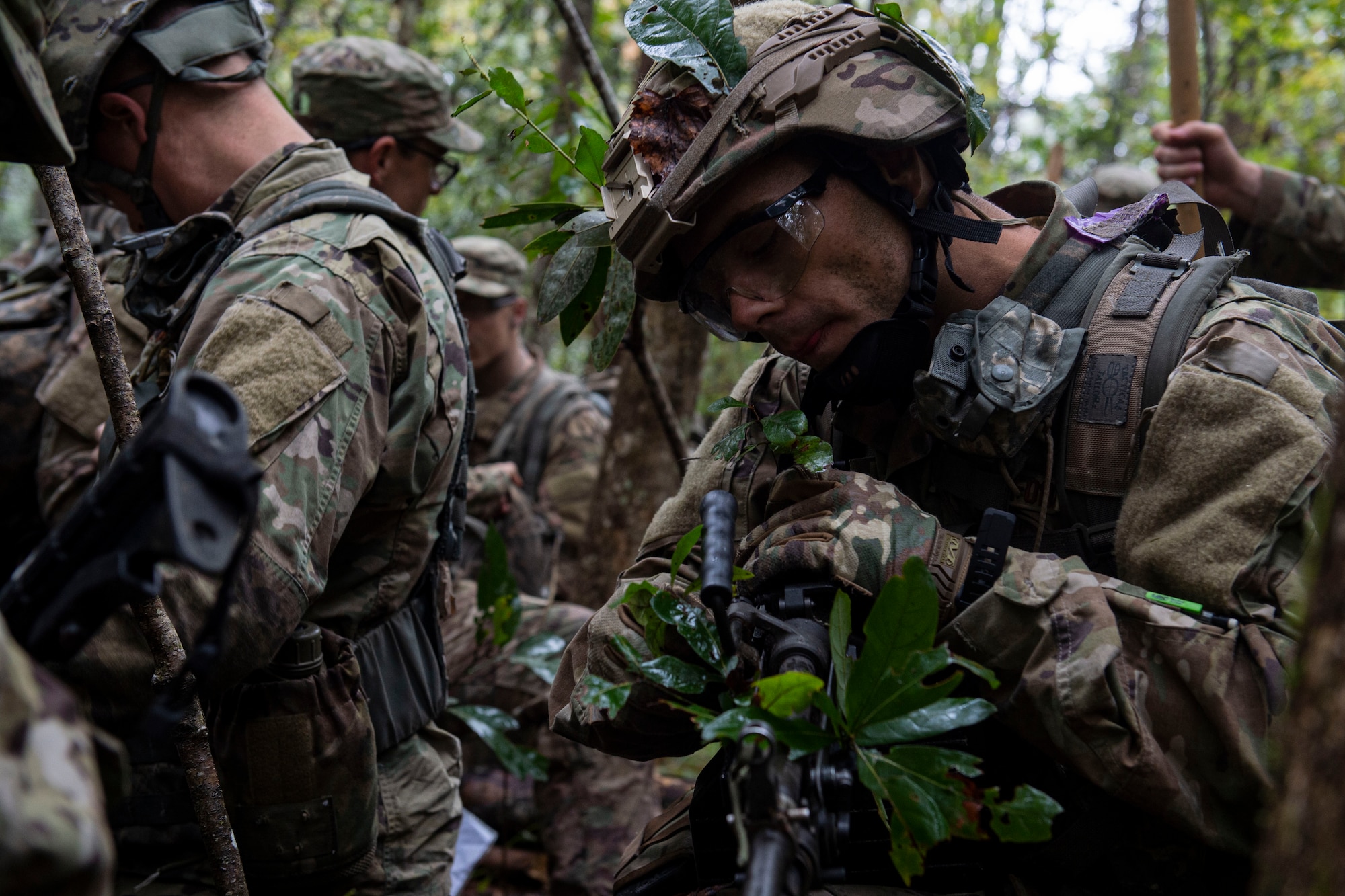 A photo of an Air Force Ranger Assessment Course student camouflaging his weapon