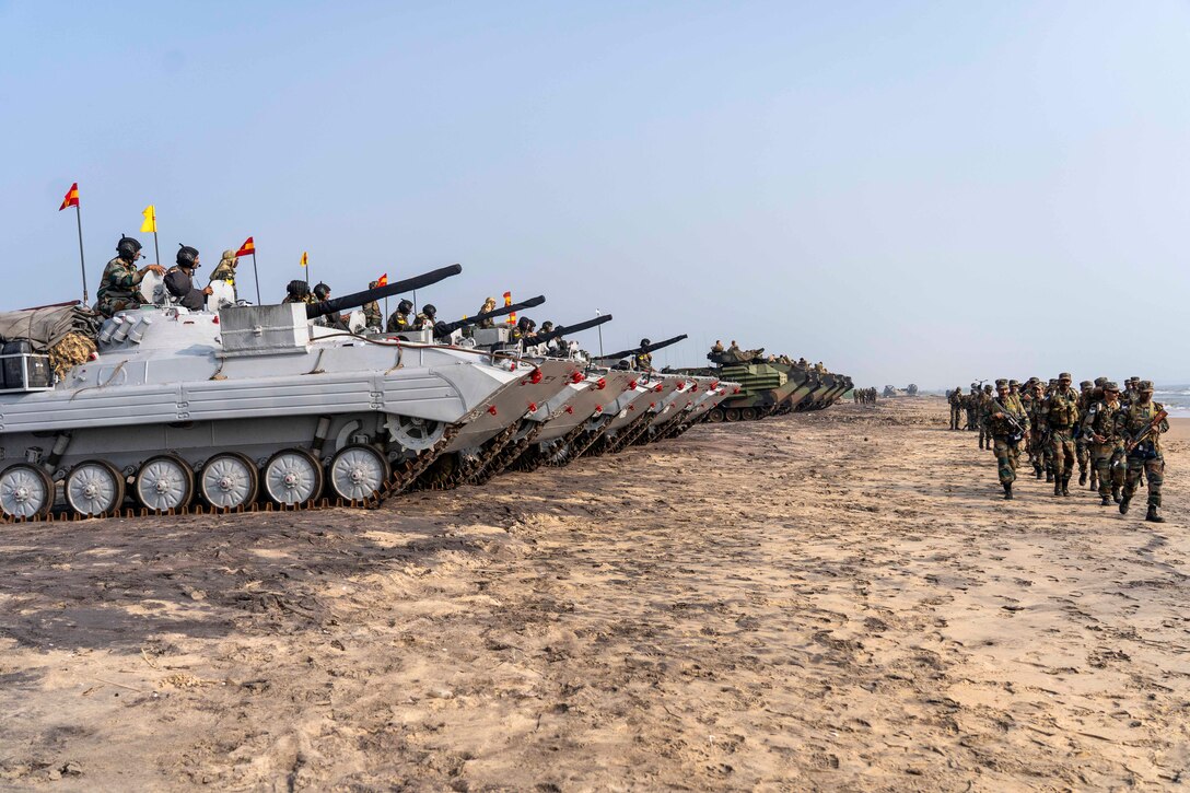 A group of Marines walk alongside a row of tanks.