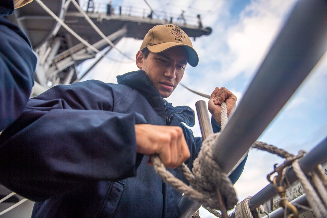 A sailor ties a rope onto a pole.