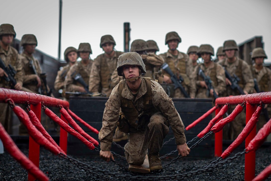 A Marine Corps recruit climbs over a chain bridge.