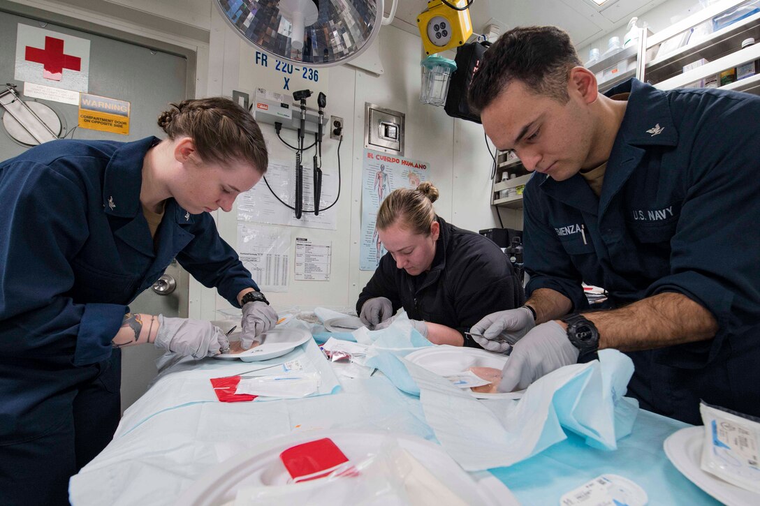 Three sailors work on a simulated patient.