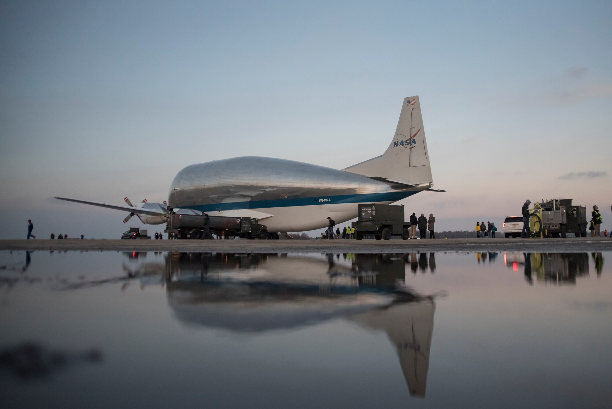A photo of the NASA Super Guppy aircraft and it's reflection, parked on the flight line after a snow shower melted