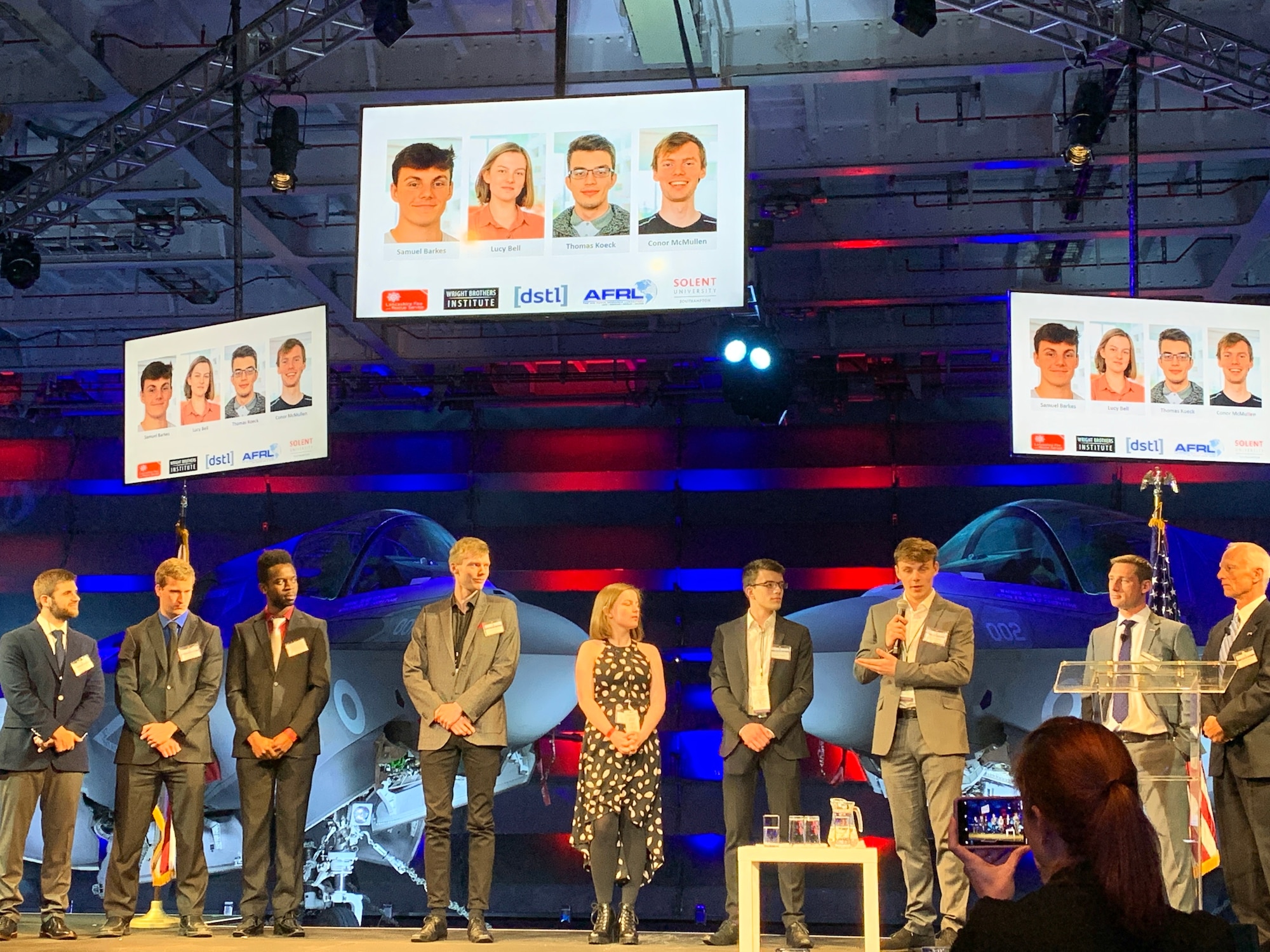 Both “Swarm and Search AI Challenge: 2019 Fire Hack” first-place teams on stage with Timothy Wright, DSTL’s Aerospace Systems Group Leader, second from right, and Mick Hitchcock, AFRL Program Manager, far right. (Courtesy photo)
