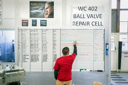 Romel Ramos, a bench mechanic with Shop 31, Inside Machine Shop, updates the status board for employees with Work Center-402 inside Building 432.