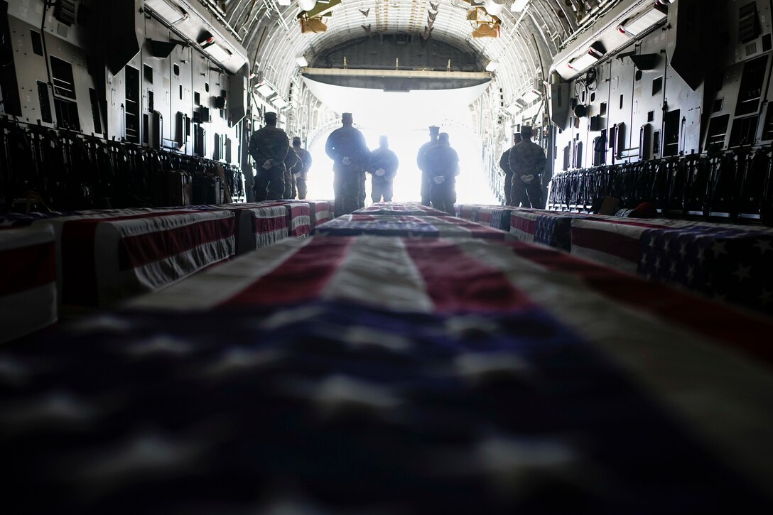 A group of people stand in front of rows of coffins draped by American flags.