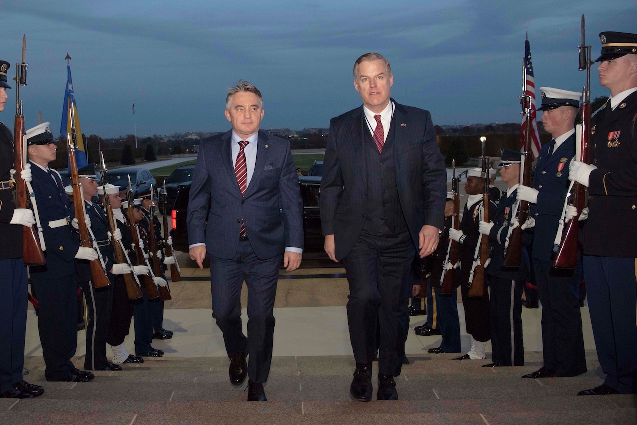 Two men walk up steps flanked by service members.