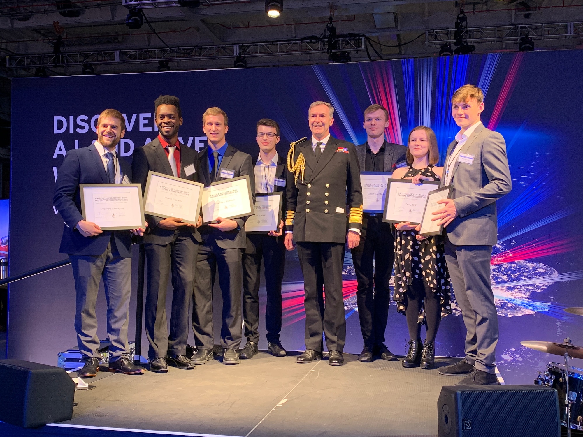 The two first-place teams from the “Swarm and Search AI Challenge: 2019 Fire Hack” were recognized during a special ceremony on board the HMS Queen Elizabeth Nov. 20, by Admiral Tony Radakin, First Sea Lord and Chief of the Royal Navy. From left, the team from the University of Michigan, including Matthew Romano, Prince Kuevor, and Jeremy Castagno. The team from the United Kingdom included Thomas Koeck, Connor McMullen, Lucy Bell, and Samuel Barkes. (Courtesy photo)