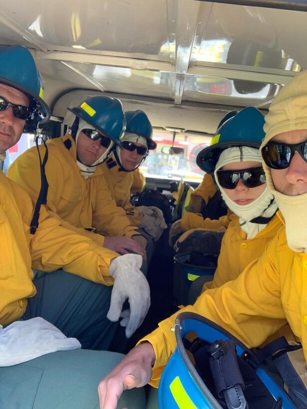 Firefighters in full firefighting gear are sitting in a vehicle.