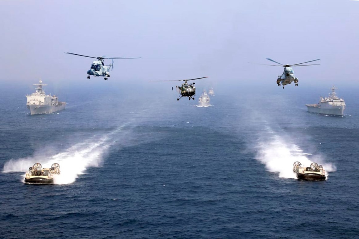 Three helicopters fly above two air-cushion landing crafts and three ships.