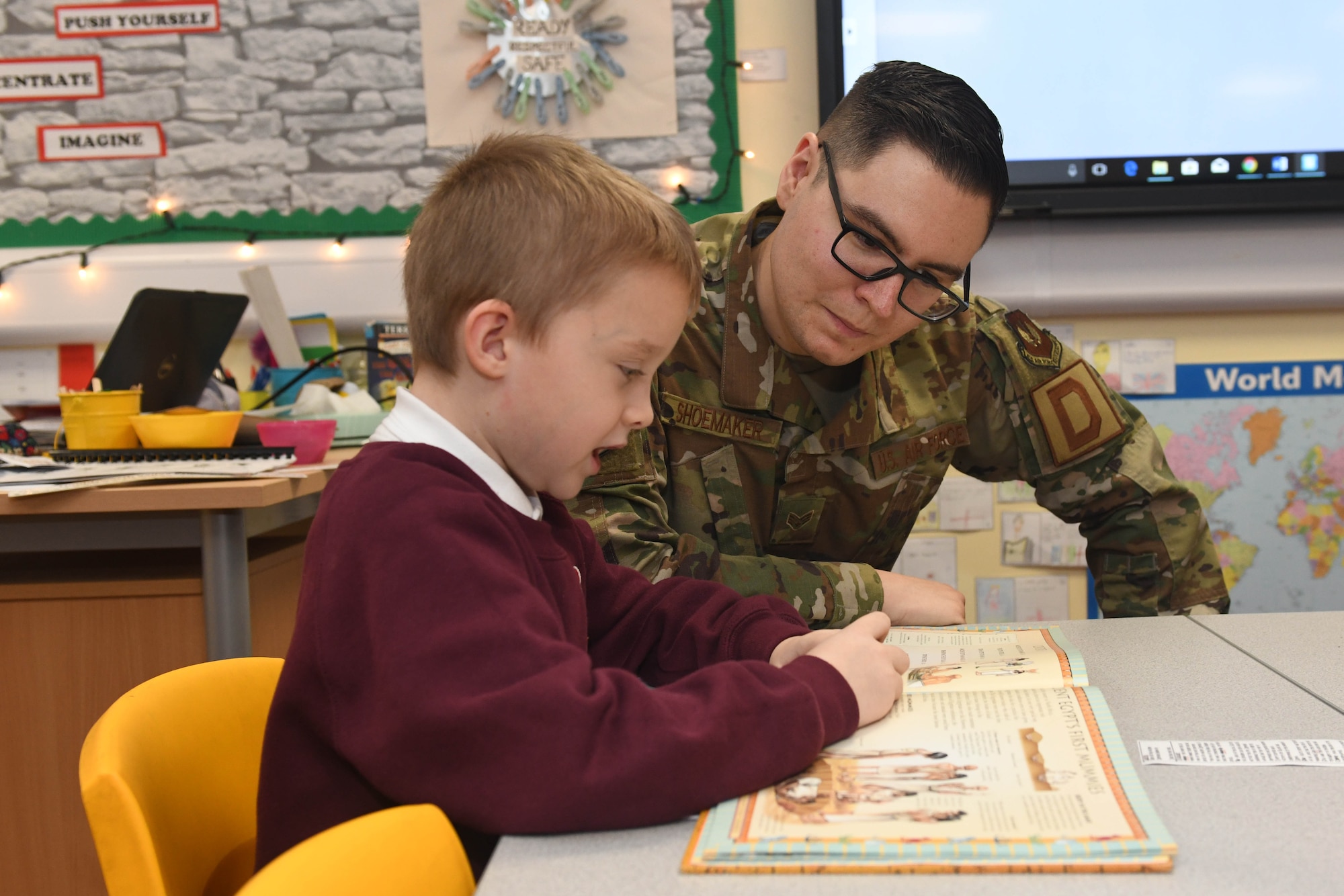 Senior Airman Andrew Shoemaker, 100th Logistics Readiness Squadron inspection apprentice, listens as a student reads a book at Houldsworth Primary School in Newmarket, England, Nov. 26, 2019. The purpose of the event was to build relations with the community while also focusing on the importance of reading for the children. (U.S. Air Force photo by Senior Airman Luke Milano)