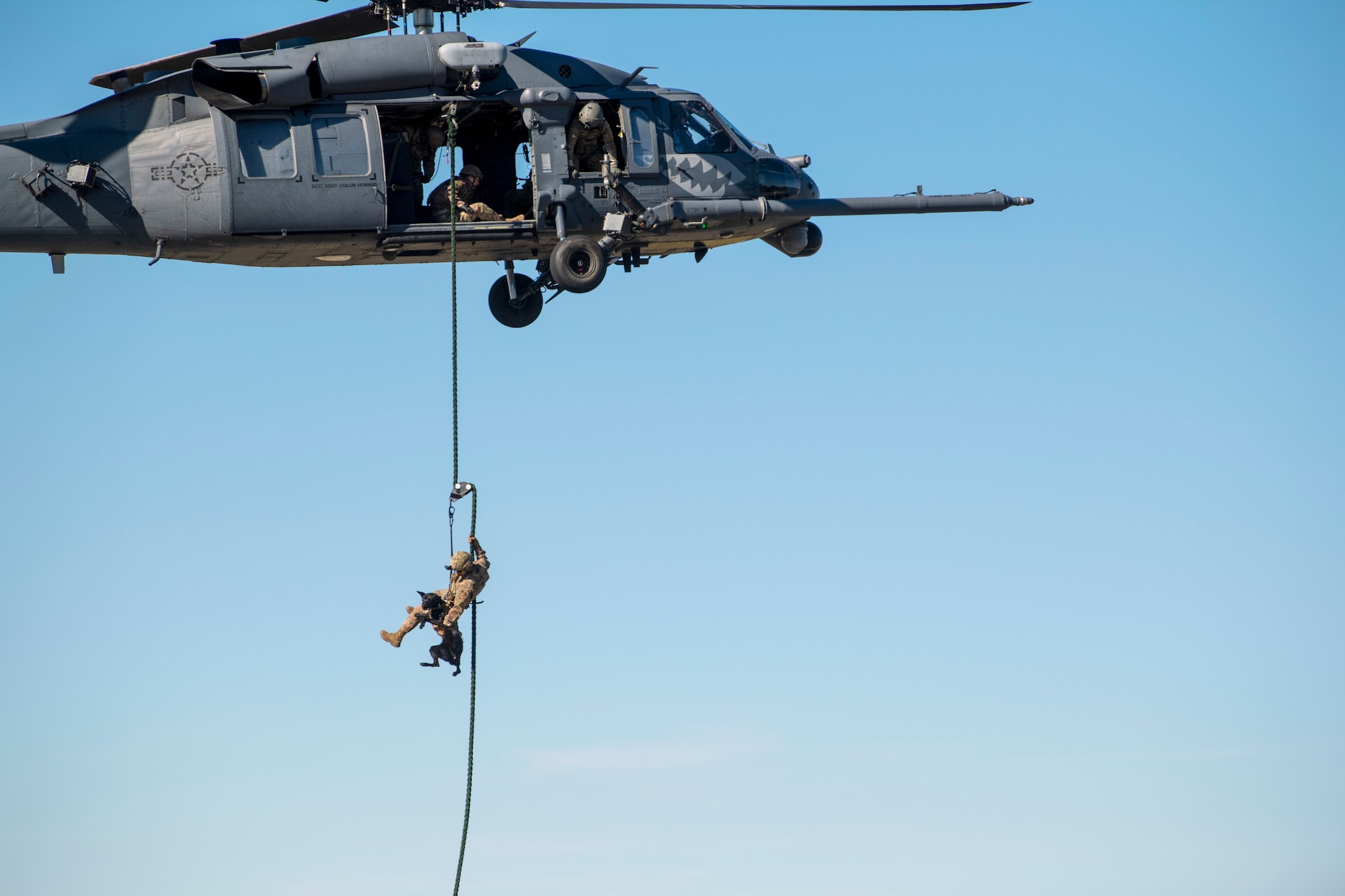 A photo of a military working dog handler fast-roping out of a helicopter with his dog