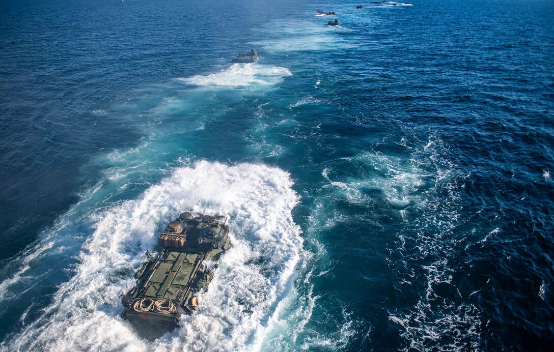 A group of amphibious assault vehicles travel through waters.