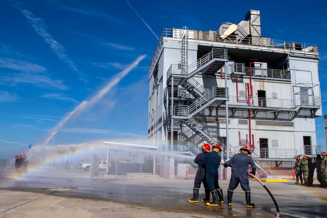 A group of sailors hold onto a water hose as it sprays a building.