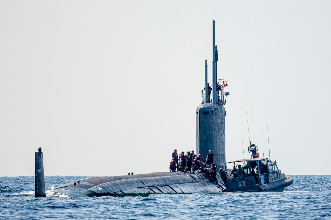 A boat next to a submarine with sailors on top.