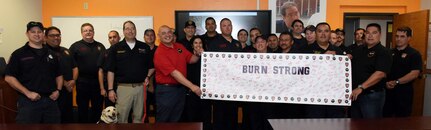 Brent Sabatino (in red shirt), U.S. Army Institute of Surgical Research Burn Center burn intensive care unit nurse, holds the banner for the Burn Strong program among first responders with the San Antonio Fire Department. The first responders attended a course instructed by Sabatino on advanced burn care that is part of the Burn Strong program, a partnership between the San Antonio Fire Department and USAISR in which paramedics and EMTs learn the basics of advanced burn and trauma life support care.