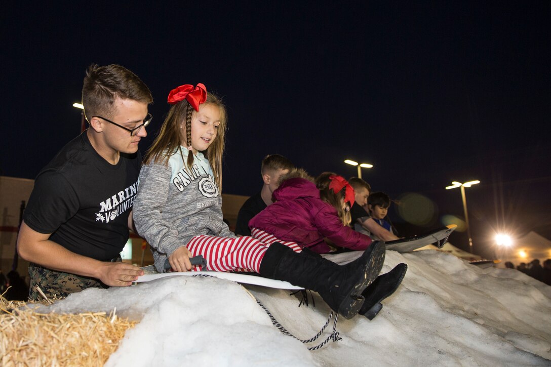 U.S. Marine Lance Cpl. Steven Champion, a volunteer for the Camp Pendleton 2019 Tree Lighting Celebration, assists children sledding down a snowy hill at the Pacific Views Marine Corps Exchange on Marine Corps Base Camp Pendleton, California, Nov. 23, 2019. The 50 foot holiday tree has over 30,000 twinkling lights and has been used for the past five years. The event also consists of a children’s carnival with games and rides, various sweepstakes, Santa and Mrs. Clause. Champion is a native of Cincinnati. (U.S. Marine Corps photo by Lance Cpl. Angela Wilcox)