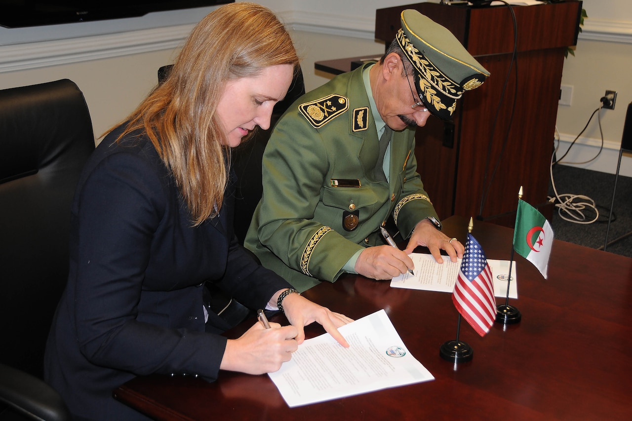 A civilian and a military officer sign documents at a table.